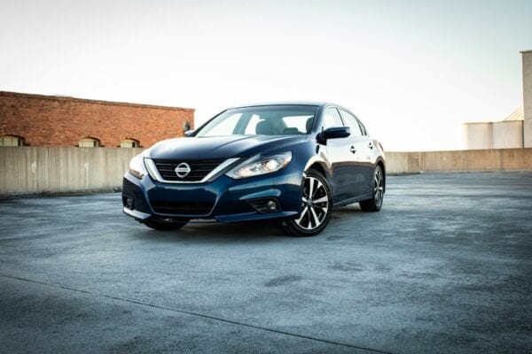 Black Nissan sedan parked on rooftop with cityscape background.
