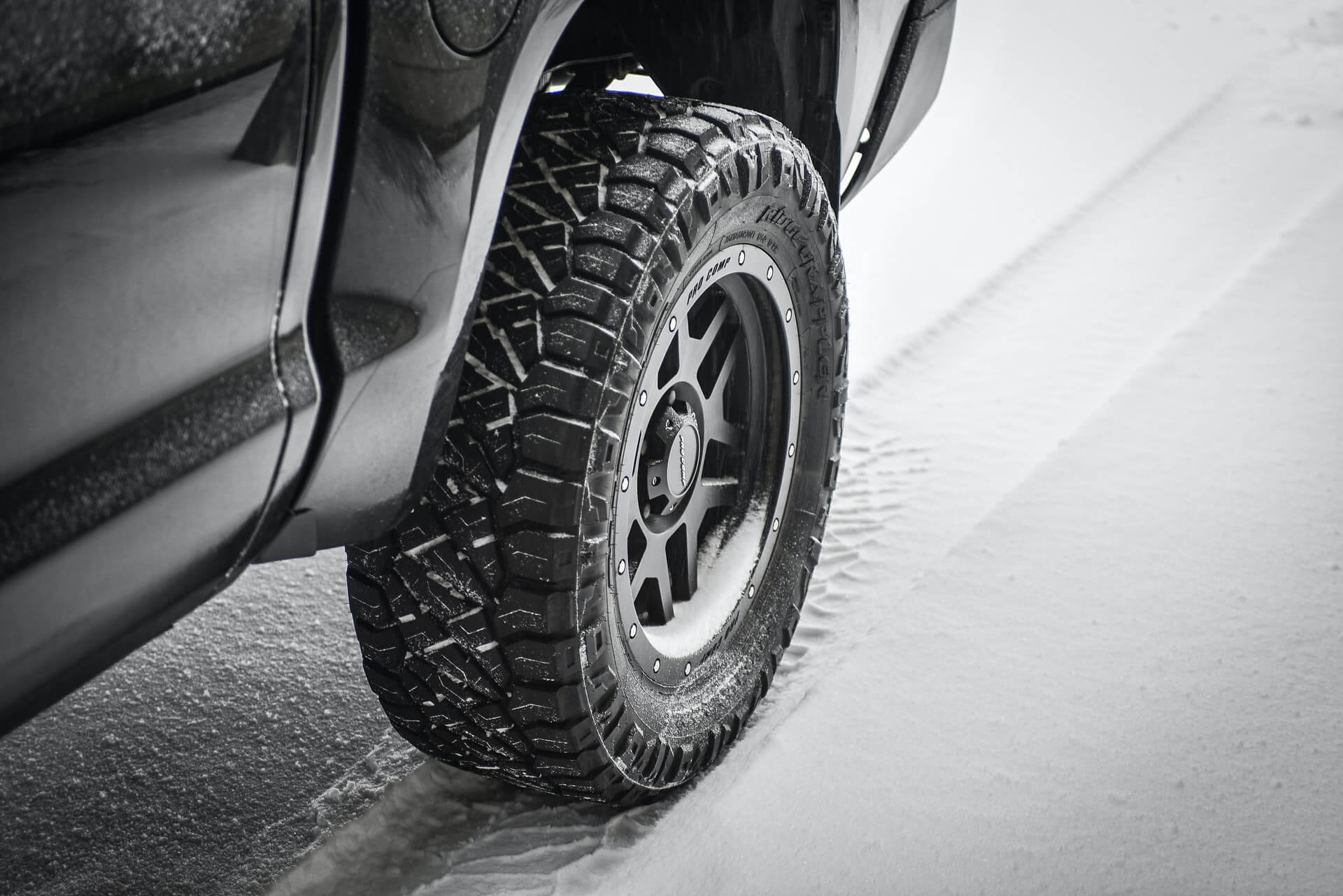Close-up of a rugged winter tire on a vehicle in snowy conditions.
