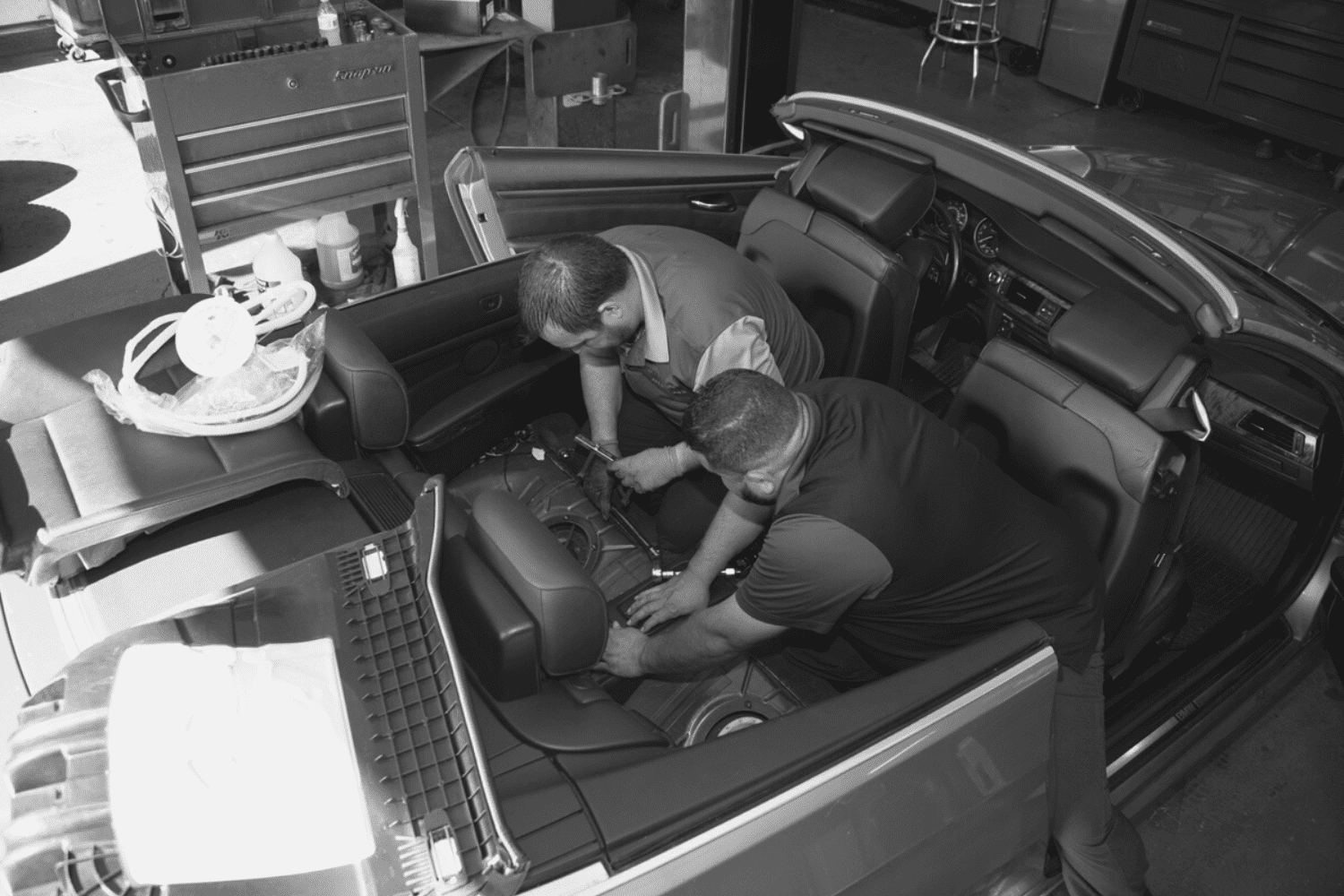 Automotive technicians inspecting and fixing a convertible car's interior components.