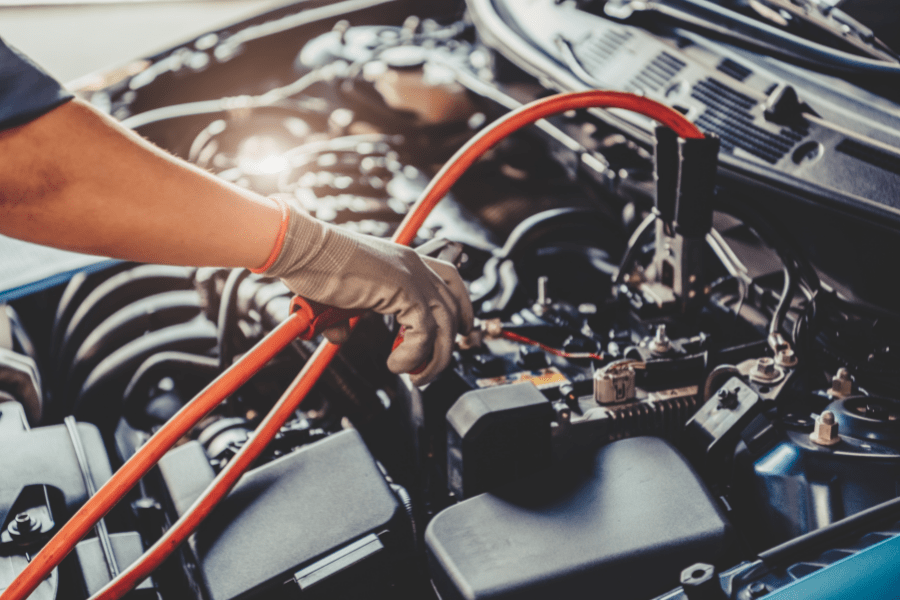 Auto electrical service technician working on car wiring and battery system.