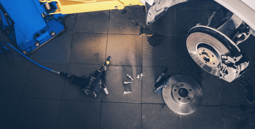 Technician inspecting brake system components on a vehicle in auto repair shop.