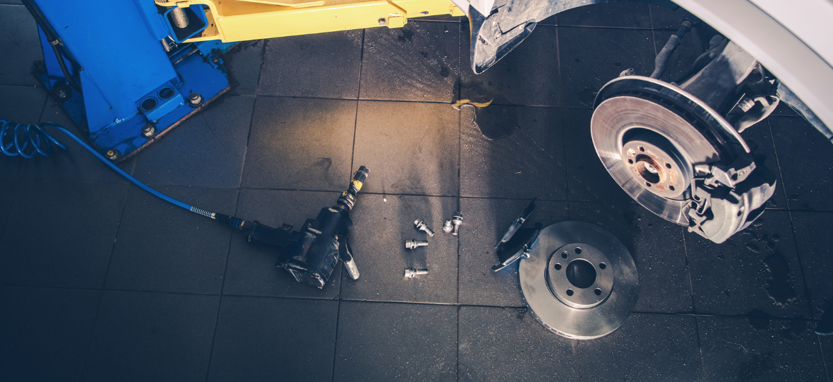 Technician inspecting brake system components on a vehicle in auto repair shop.