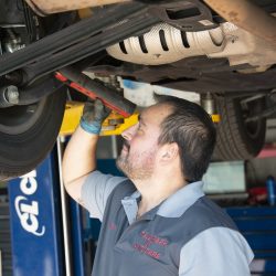 Auto repair technician checking under car for maintenance or repairs.