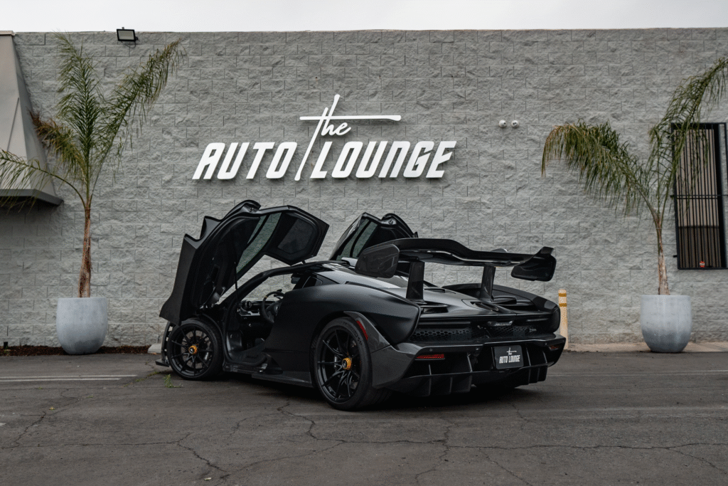 Luxury black sports car with open doors parked in front of The Auto Lounge sign. Perfect for car ent.