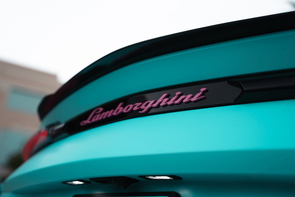 Close-up of a turquoise Lamborghini with pink logo at The Auto Lounge.