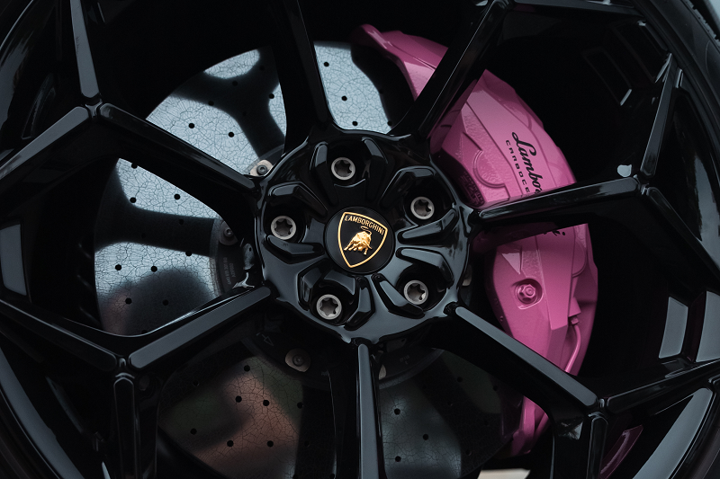 Lamborghini wheel with pink brake caliper and black rim.