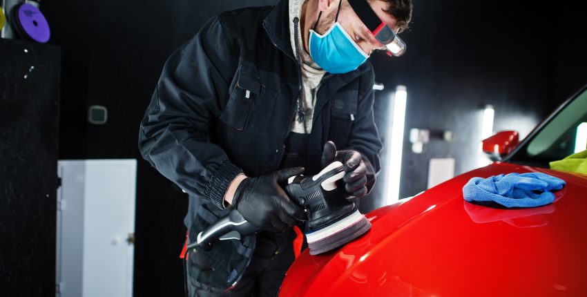 Automotive technician applying paint protection film to a red vehicle.