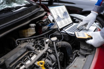 Technician using diagnostic tools on car engine with laptop and scanner for vehicle analysis.