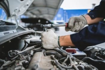 Engine repair technician working on car engine with wrench in auto repair shop.