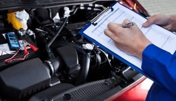 Technician inspecting car engine with clipboard during vehicle service.