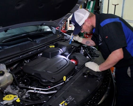 Automotive mechanic inspecting engine bay for maintenance or repairs.