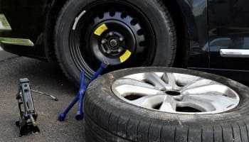 Car tire being replaced with a spare tire on the roadside.