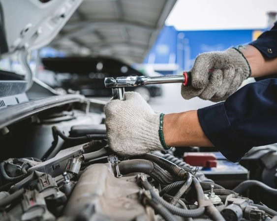 Engine repair technician working on car engine with screwdriver.