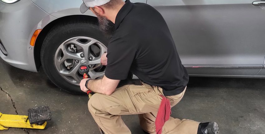 Technician repairing a silver car in an auto repair shop.