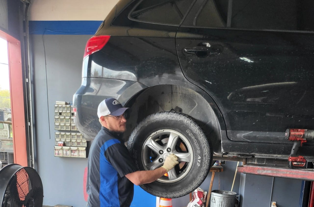 Technician repairing a black SUV's rear wheel in the garage.