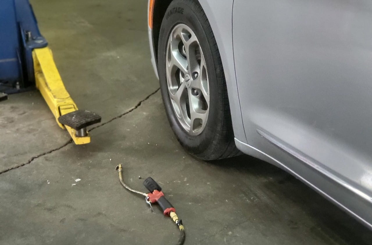 Automotive tire repair equipment near a silver car in a garage.