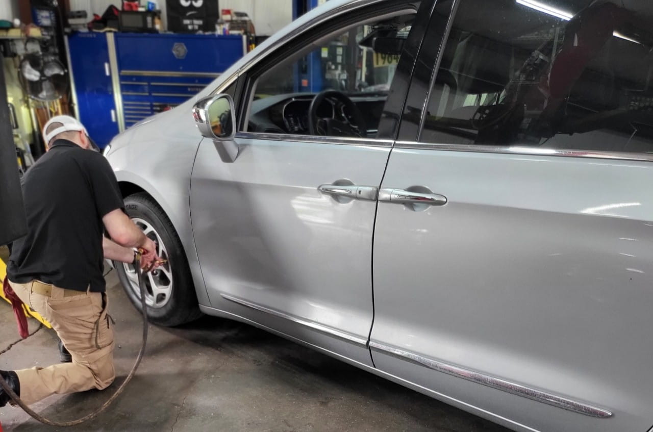 Technician inspecting a silver minivan in auto repair shop.