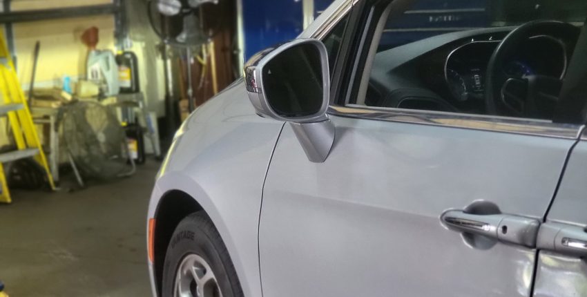Silver car parked inside a garage with tools and equipment in background.
