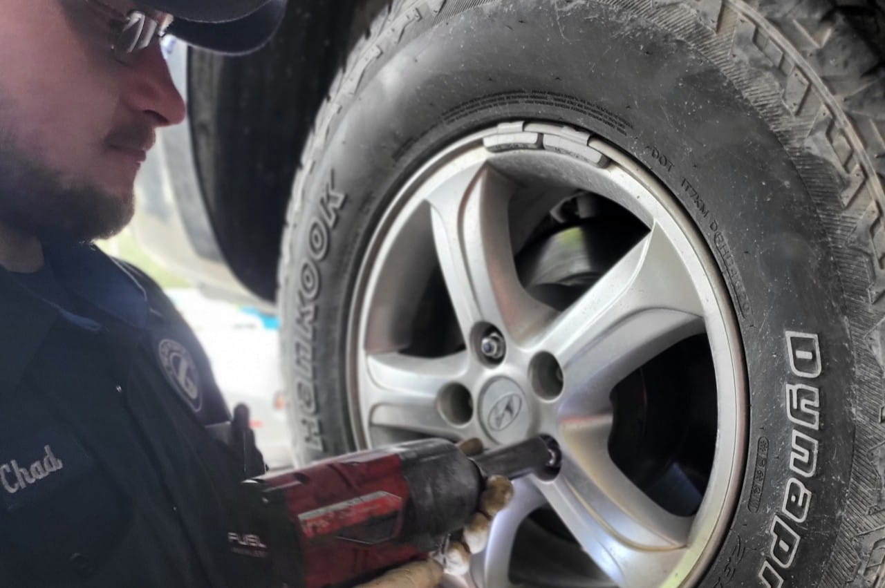 Technician inspecting a car tire with a power tool at The Car People.