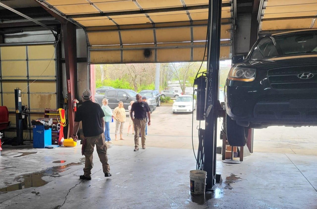 Auto repair shop with cars, customers, and mechanics working inside.