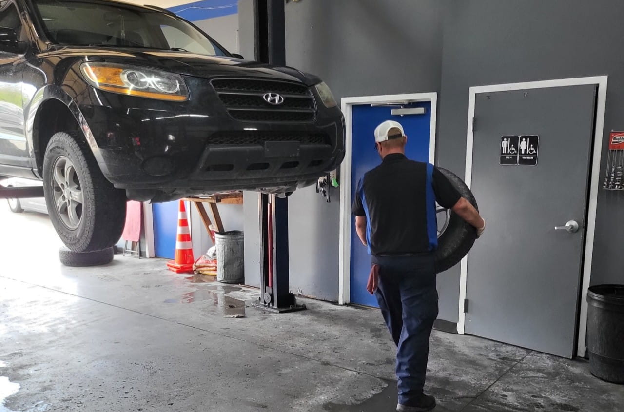 Black SUV on car lift at auto repair shop with mechanic.