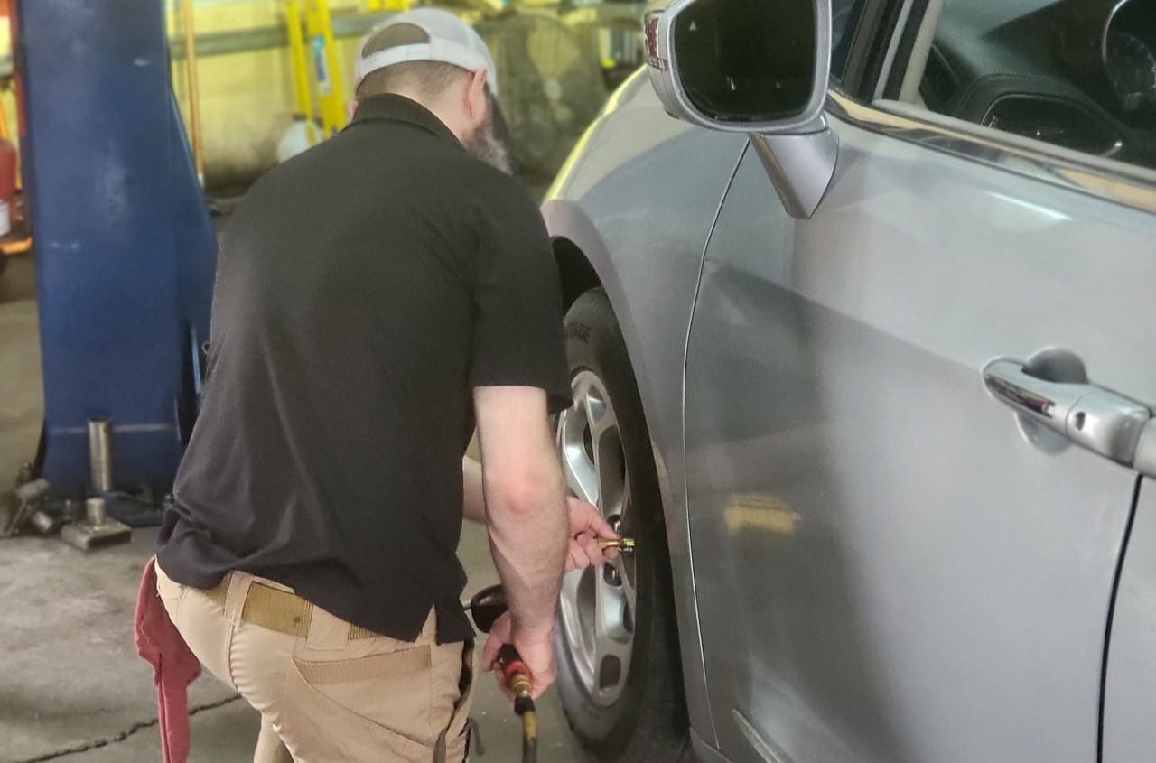 Technician inspecting a car tire at The Car People auto shop.
