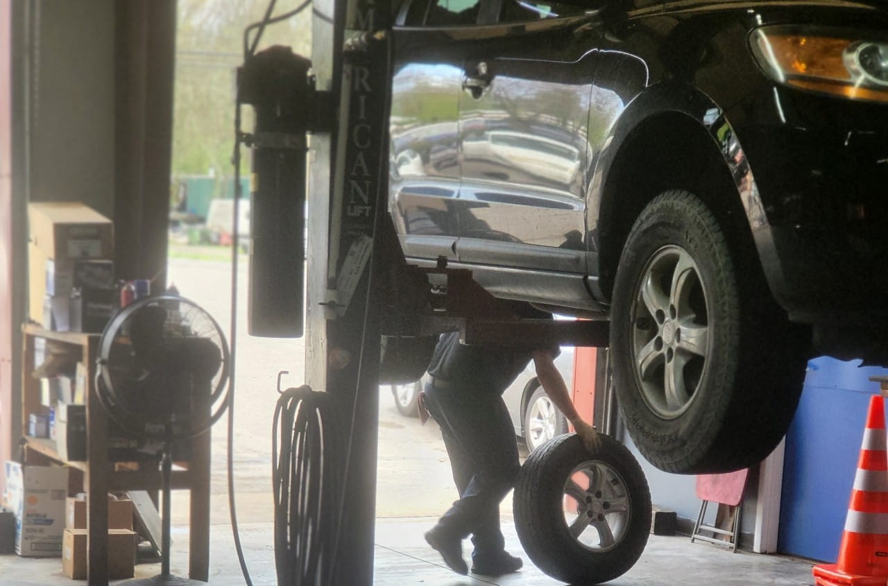 Black car lifted on hydraulic lift at auto repair shop.