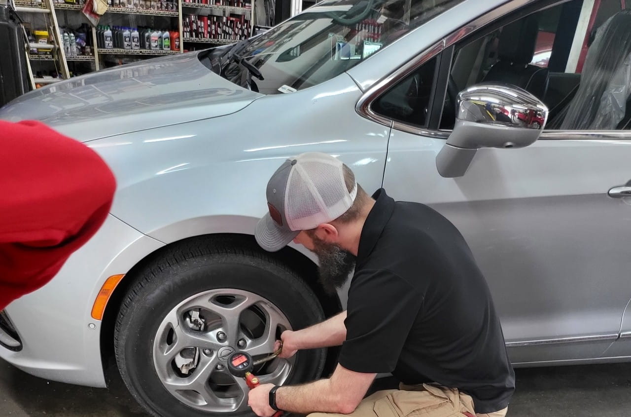 Technician inspecting a silver car's wheel at The Car People.