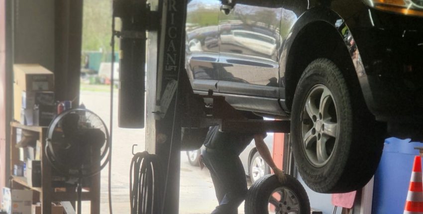 Black car lifted on hydraulic lift at auto repair shop.