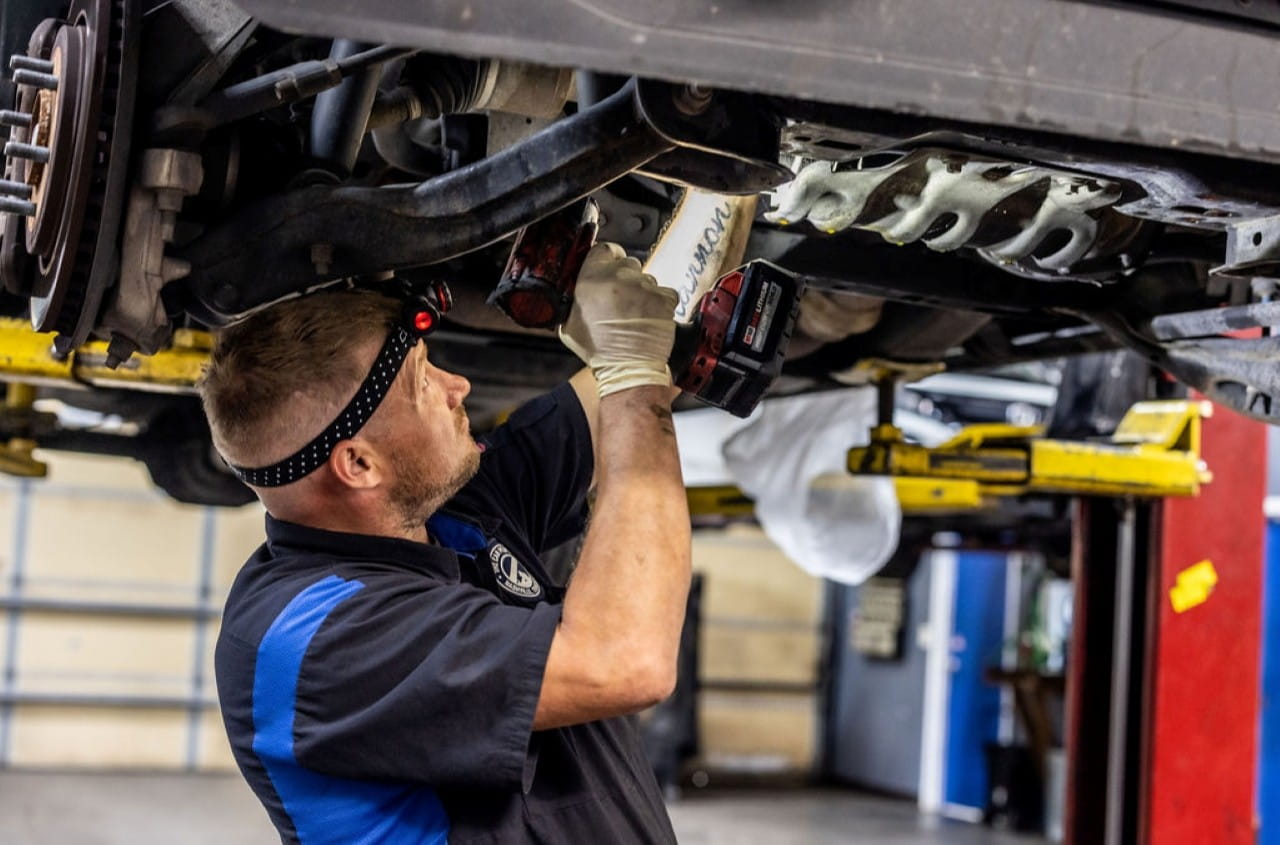 Auto mechanic inspecting vehicle underside in repair shop.
