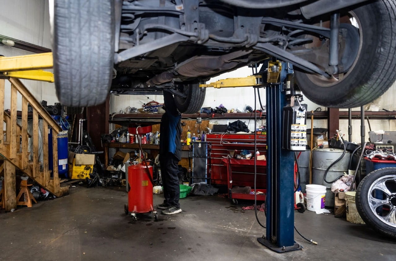 Mechanic inspecting car lifted on hydraulic lift in auto repair shop.
