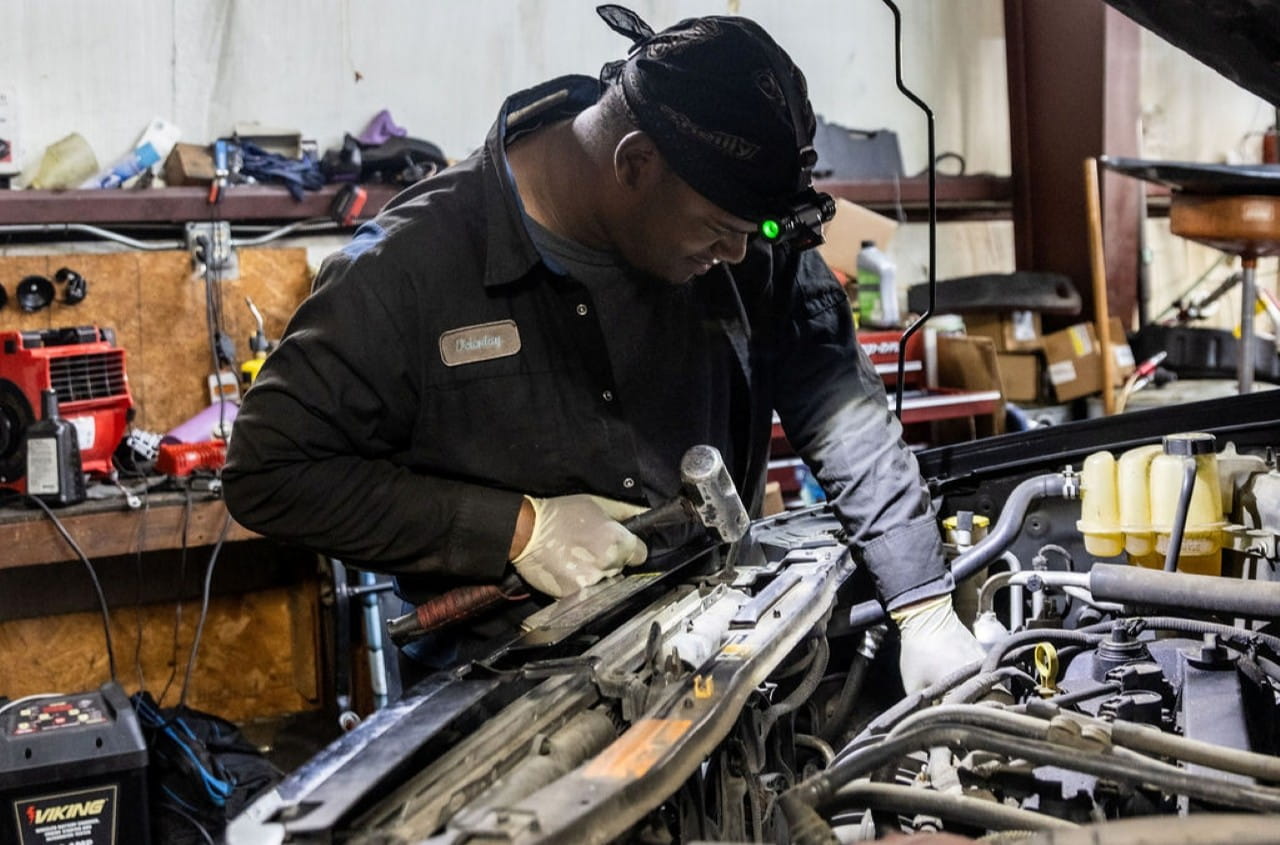 Auto mechanic repairing car engine in garage with tools and equipment.