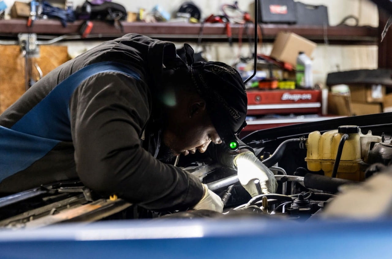 Mechanic inspecting car engine in garage for maintenance or repair.