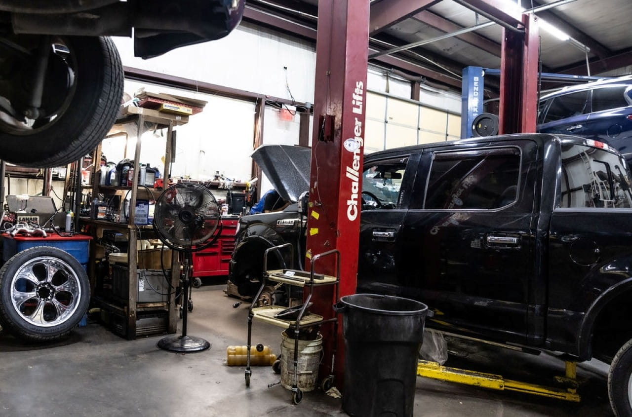 Black SUV on lift in auto repair shop with tools and equipment.