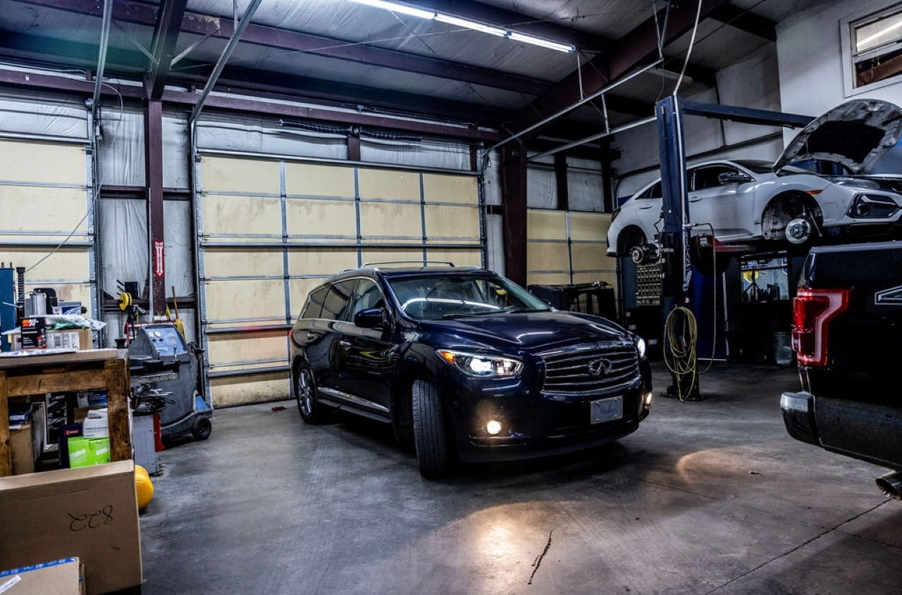 Black Infiniti sedan inside an auto repair shop with car lift and tools.