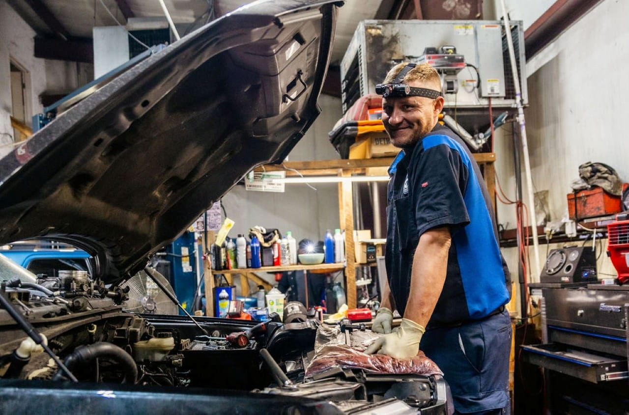 Automotive technician inspecting car engine in repair shop.