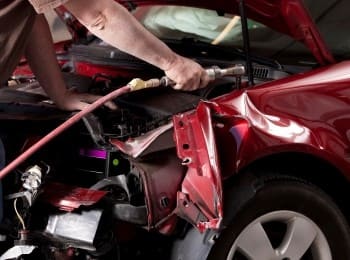 Auto body repair technician working on a red car after a collision.