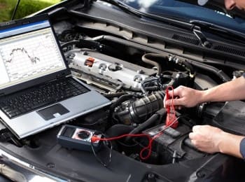 Car battery testing with diagnostic tools and a laptop under the hood.