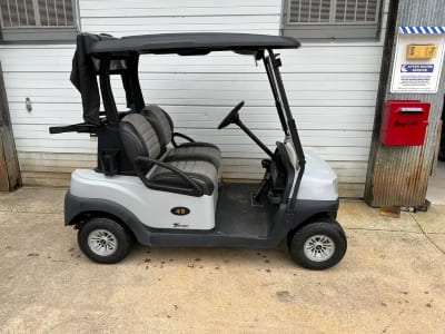 Golf cart with black roof and seating for four, parked outside a building.