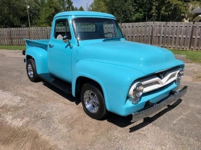 Vintage blue pickup truck parked outdoors with a wooden fence in the background.