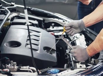 Technician repairing car engine with tools in auto repair shop.