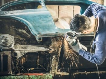 Auto mechanic grinding rust on vintage car frame with angle grinder.