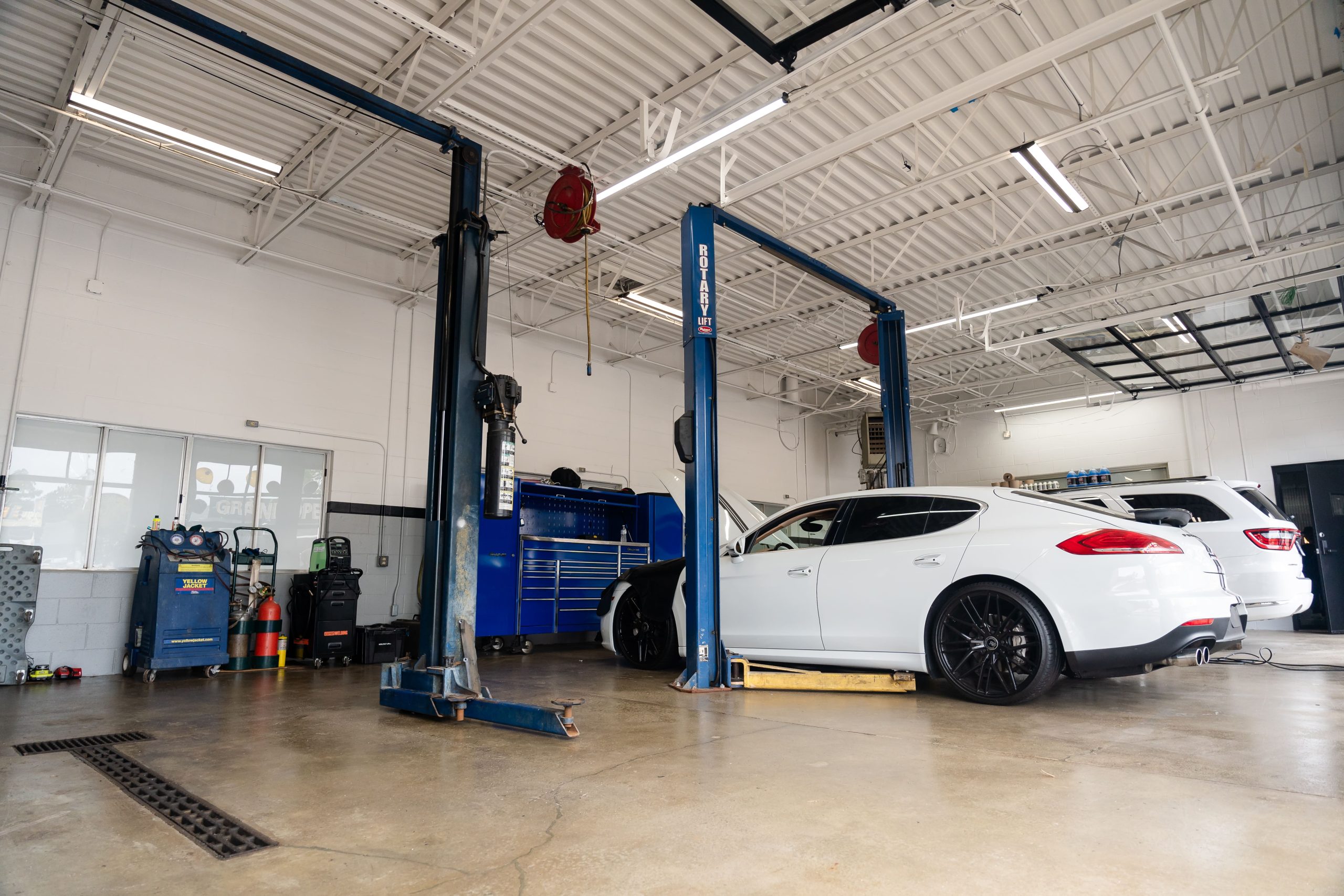 Car repair shop with a white luxury vehicle on a hydraulic lift.