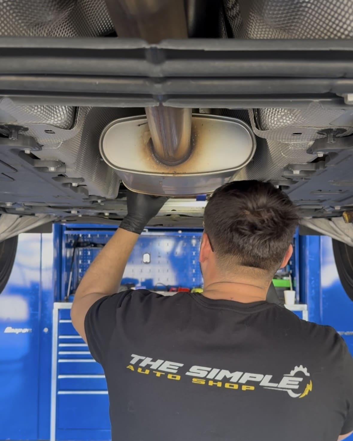 Auto repair technician inspecting vehicle exhaust system in garage.