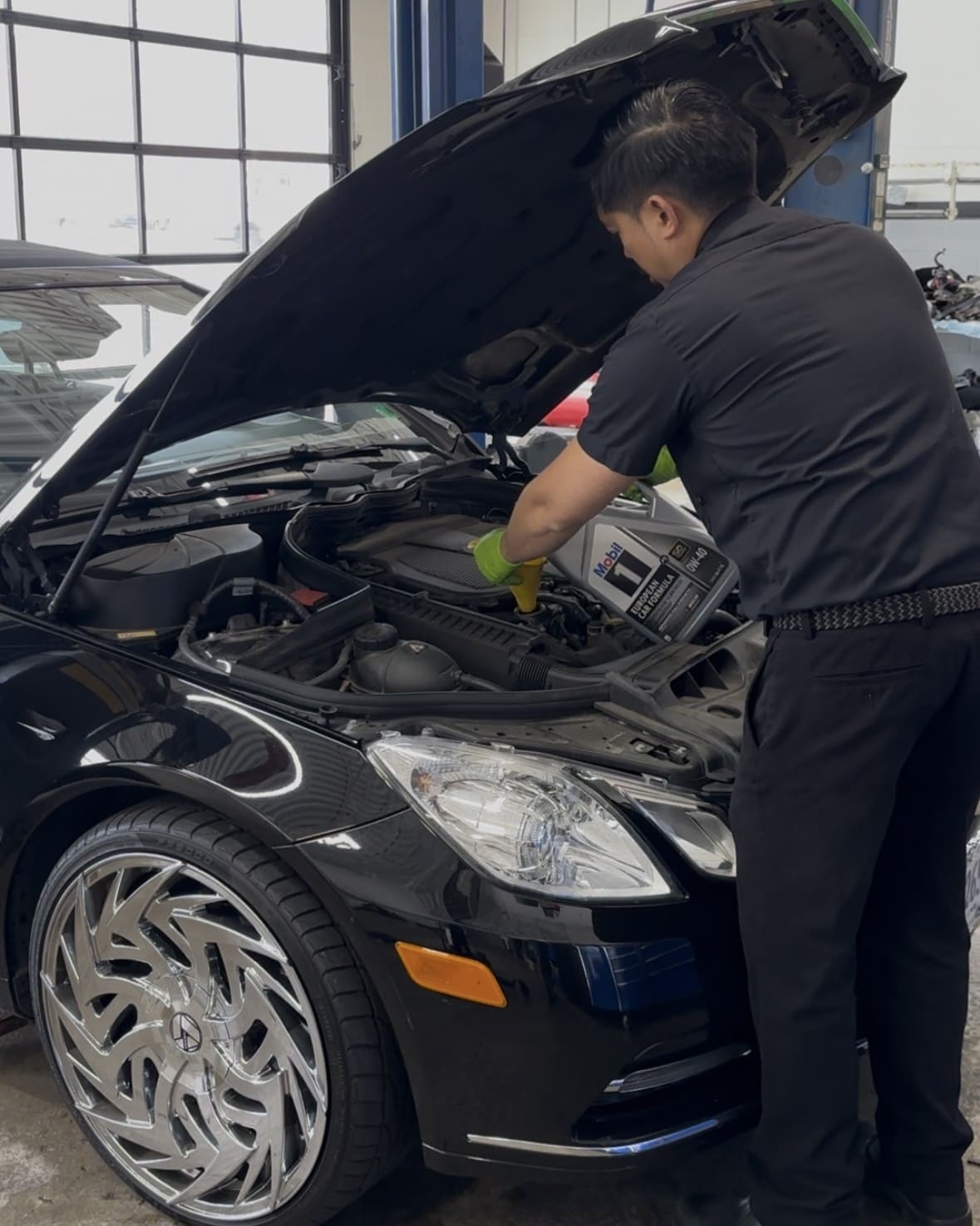 Auto mechanic inspecting a car engine with open hood.