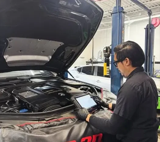 Technician inspecting car engine with diagnostic tool at auto repair shop.