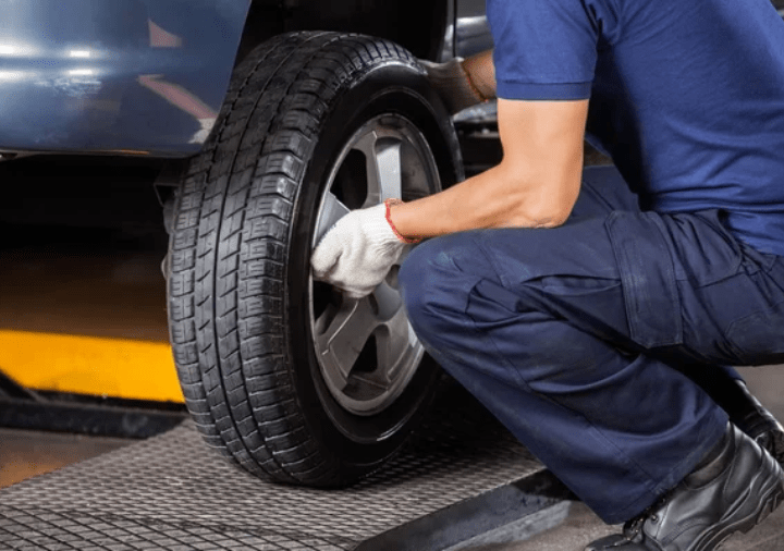 Technician inspecting tire tread for wear and safety on a vehicle.