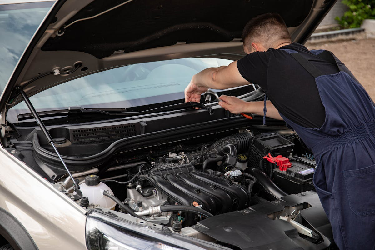 Engine diagnostics technician working on vehicle electronics under the hood.