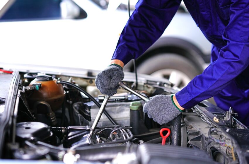 Engine repair technician working on a car engine with tools in hand.