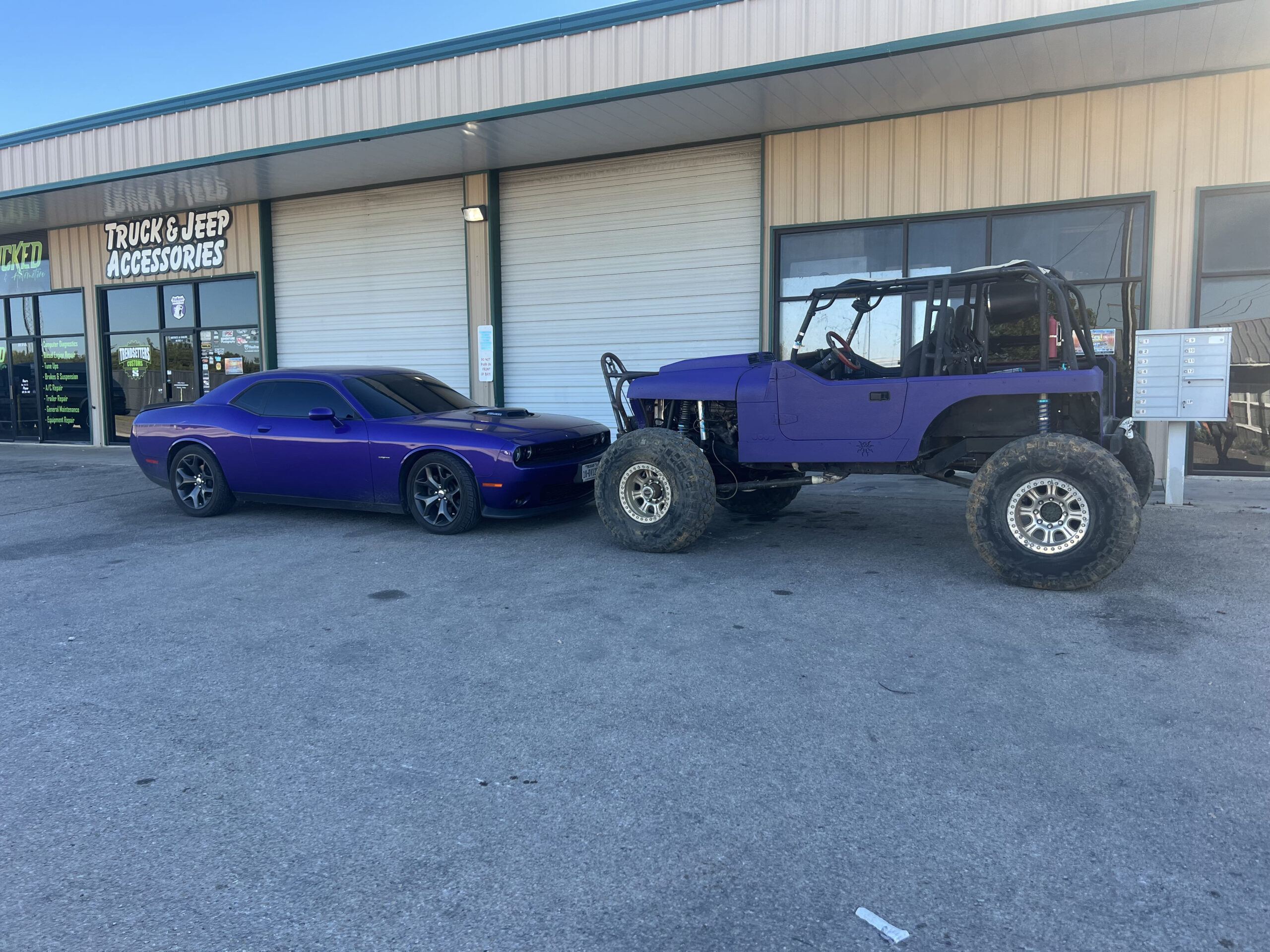 Custom painted purple Dodge Challenger and rugged off-road Jeep parked outside Trendsetters Customs.